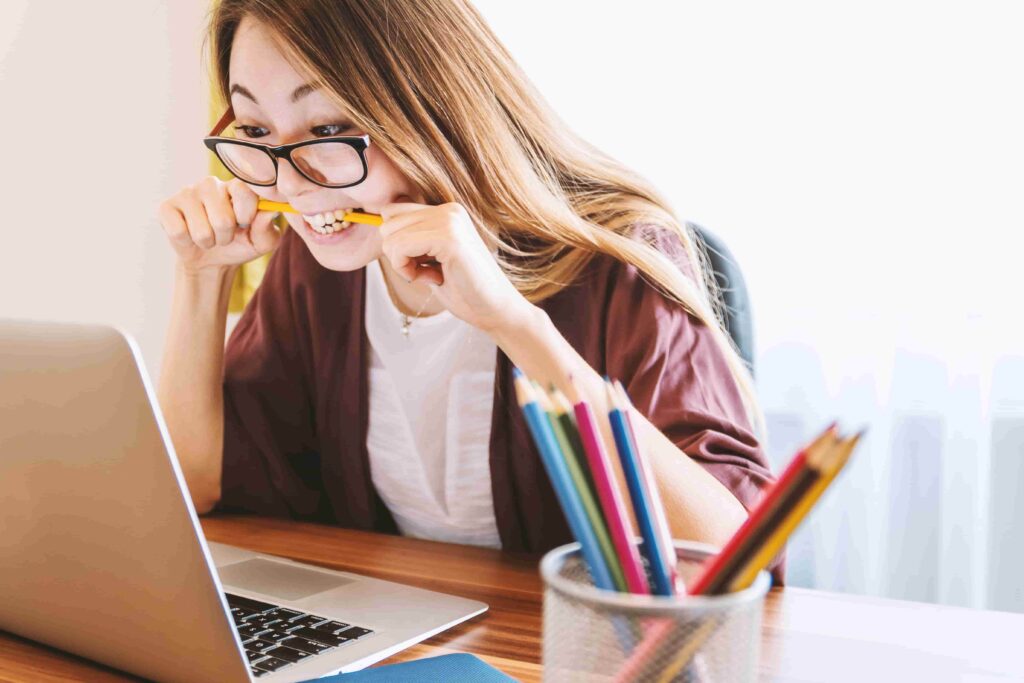woman biting pencil while sitting on chair in front of computer during daytime-min